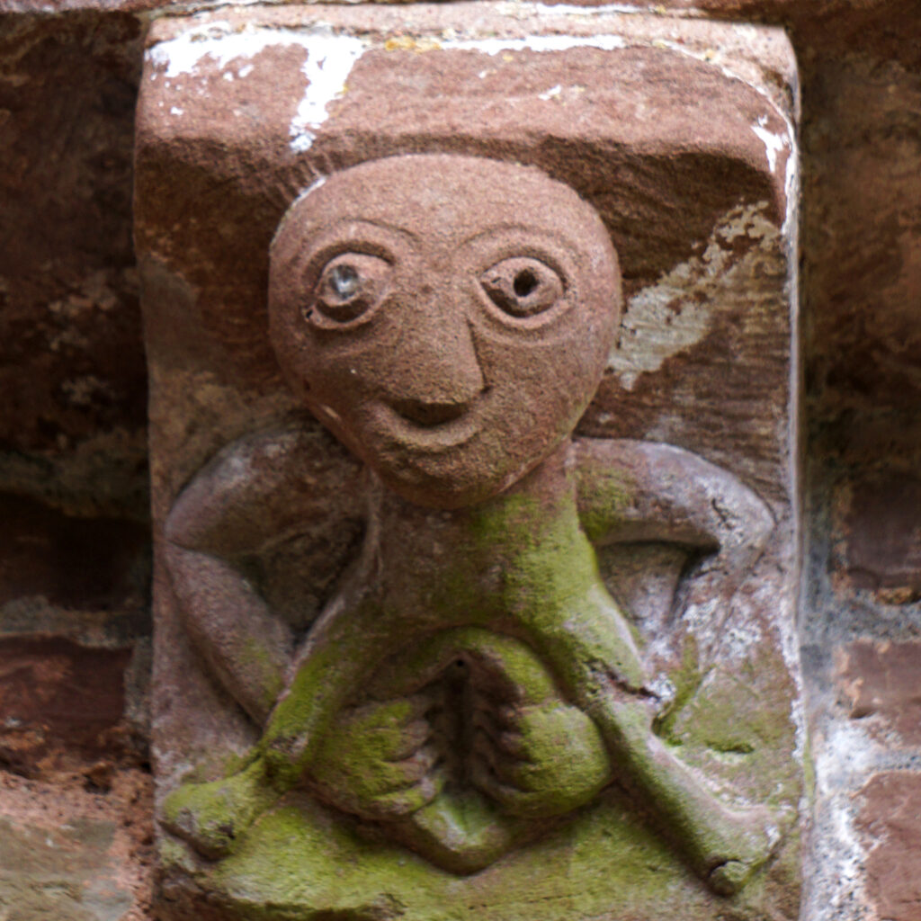 A crude stone carving of a human figure reaching down to spread an oversize vagina