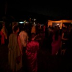 Guests at the first Pennsic Knowne World Courtesans Roman Bacchanal on August 7th, 2017 People in ancient Roman clothing standing and sitting while drinking, eating, and chatting outdoors at night