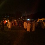 Guests at the first Pennsic Knowne World Courtesans Roman Bacchanal on August 7th, 2017 People in ancient Roman clothing standing and sitting while drinking, eating, and chatting outdoors at night