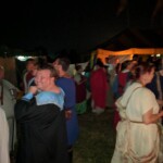 Guests at the first Pennsic Knowne World Courtesans Roman Bacchanal on August 7th, 2017 People in ancient Roman clothing standing and sitting while drinking, eating, and chatting outdoors at night