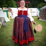 Courtesan Lucrezia Ridolfi posing as she arrives at the Pennsic Knowne World Courtesans Social on August 10, 2017 A woman dressed in Renaissance clothing smiling and holding a wine glass, a fan, and a purse