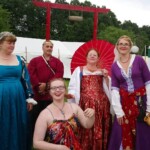 Courtesans Oriana of Xylina, Magdalena la Sanguigni, Margaret of Buckrode, and Fioré al-Rumi posing with a friend as they arrive at the Pennsic Knowne World Courtesans Social on August 10, 2017 Five people wearing medieval and Renaissance clothing posing together