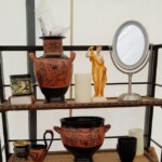 Aphrodite for the altar to Venus, the amphora, the scoop and the wine bowl awaiting the 2018 Bacchanal A shelf holding various items including replicas of an ancient Greek wine bowl, scoop, and amphora, as well as a statuette of Aphrodite, a mirror, a mug, and fake candles