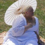 Courtesan Fortune St Keyne posing at Pennsic in August of 2012 A woman in Italian Renaissance clothing relaxing on a blanket on the grass and holding a white parasol