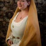 Courtesan Bianca Anguissola at the Annual KWC Social at Pennsic in August of 2015 A person in Italian Renaissance clothing smiling and holding a hand fan in front of an old fashioned map background