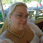 Courtesan Fortune St Keyne at Pennsic in August of 2015 Closeup of a woman in Italian Renaissance clothing with picnic tables, a road, and medieval style tents in the background