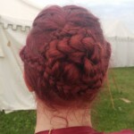 Courtesan Bianca Anguissola showing off her hairstyle before the first Pennsic Knowne World Courtesans Roman Bacchanal on August 7th, 2017<br><br>Hairstyle by Lucretia Marcella Closeup of the back of the head of a woman in ancient Roman clothing with an intricate updo hairstyle in front of some medieval style tents