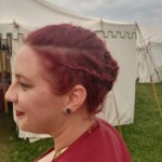 Courtesan Bianca Anguissola showing off her hairstyle before the first Pennsic Knowne World Courtesans Roman Bacchanal on August 7th, 2017<br><br>Hairstyle by Lucretia Marcella Closeup of a woman in ancient Roman clothing with an intricate updo hairstyle looking to the side in front of some medieval style tents