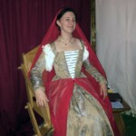 Courtesan Ginevra Fiammetta di Silvestri prepares to attend the Casa Bardicci's Hoity Toity party at Pennsic on August 10, 2017 A woman in 16th century Venetian clothing and a red veil sitting on a medieval style chair inside a medieval style tent