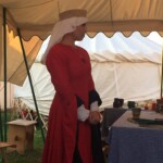 Courtesan Esa inghean Donnchaidh at her apprentice ceremony to Beatriz Aluares de la Oya at Pennsic on August 3, 2017 A woman in medieval clothing standing inside a medieval style tent and looking to the side