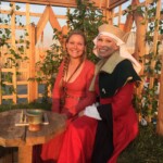 Courtesan Esa inghean Donnchaidh with patron Margaret Lad at Esa's apprentice ceremony to Beatriz Aluares de la Oya at Pennsic on August 3, 2017 Two people in medieval clothing sitting in a medieval garden behind a small table and smiling