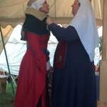 Courtesan Esa inghean Donnchaidh with her Laurel Beatriz Aluares de la Oya at their apprentice ceremony at Pennsic on August 3, 2017 A person in medieval clothing adjusting the hood of another person in medieval clothing inside a medieval style tent