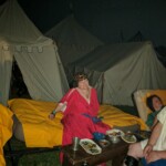 Courtesan Oriana of Xylina at the first Pennsic Knowne World Courtesans Roman Bacchanal on August 7th, 2017 A woman in ancient Roman garb lounging on a daybed at night outdoors. In front of her is a bench containing several plates of food.