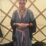 Courtesan Ginevra Fiammetta di Silvestri at Pennsic on August 3, 2018 A woman in ancient Roman clothing wearing a red veil standing with her hands crossed in front of her inside a yurt