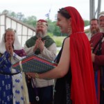 Courtesan Ginevra Fiammetta di Silvestri at Ruby Joust in Atlantia on May 27th, 2023
<br><br>Photo by Tannis of Tir-y-Don A woman in ancient Roman clothing wearing a red veil and a medallion standing in front of other people in medieval clothing who are clapping