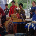 Courtesan Ginevra Fiammetta di Silvestri at Ruby Joust in Atlantia on May 27th, 2023
<br><br>Photo by Tannis of Tir-y-Don A woman in ancient Roman clothing wearing a red veil covering her mouth and kneeling in front of two people in medieval clothing wearing crowns sitting on thrones with other people in medieval clothing standing behind them
