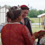 Courtesan Ginevra Fiammetta di Silvestri receives her scroll for the Order of the Pearl at Ruby Joust in Atlantia on May 27th, 2023
<br><br>Photo by Tannis of Tir-y-Don A woman in medieval clothing and a crown showing a framed piece of artwork to a smiling woman in ancient Roman clothing and a red veil
