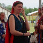 Courtesan Ginevra Fiammetta di Silvestri at Ruby Joust in Atlantia on May 27th, 2023
<br><br>Photo by Tannis of Tir-y-Don A woman in ancient Roman clothing wearing a red veil and a medallion brushing her hair out of her face and standing in front of other people in medieval clothing