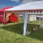 Setup in Courtesan Camp at Pennsic in Æthelmearc on August 30, 2023 View of a courtyard of a medieval style camp in which are tents and canopies with various furnishings on the ground