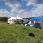 Setup in Courtesan Camp at Pennsic in Æthelmearc on August 30, 2023 View of a courtyard of a medieval style camp in which are tents and canopies with various furnishings on the ground