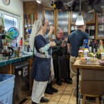 Tullians Danyel and Gamyl of Mottrum with Henrik Der Herzhaft at the Company of the Golden Fox's salon in Caid on February 25, 2023.
<br><br>
Visit the Company of the Golden Fox (Calafia Courtesans Guild) Facebook group here: <a class='blue-link' href="https://www.facebook.com/groups/540612268076159">Facebook link</a> Four people in medieval and Renaissance clothing in a modern kitchen eating, drinking, and chatting